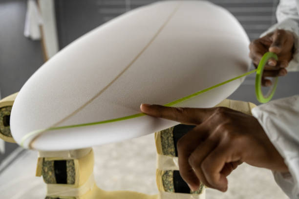 Shaping a blank surfboard with a green tape detail.