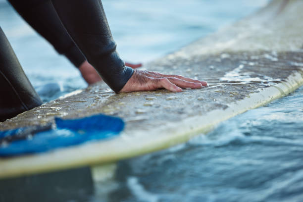 Surfer's hands pushing off a wet surfboard in the ocean, preparing to stand.