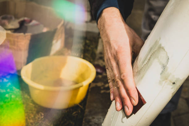 Hand sanding a damaged surfboard repair with sandpaper.